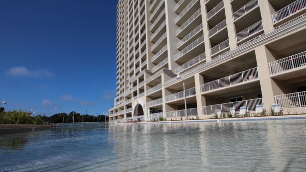 Un hôtel de grande hauteur doté de nombreux balcons, d’une piscine et surplombant un ciel d’un bleu limpide.