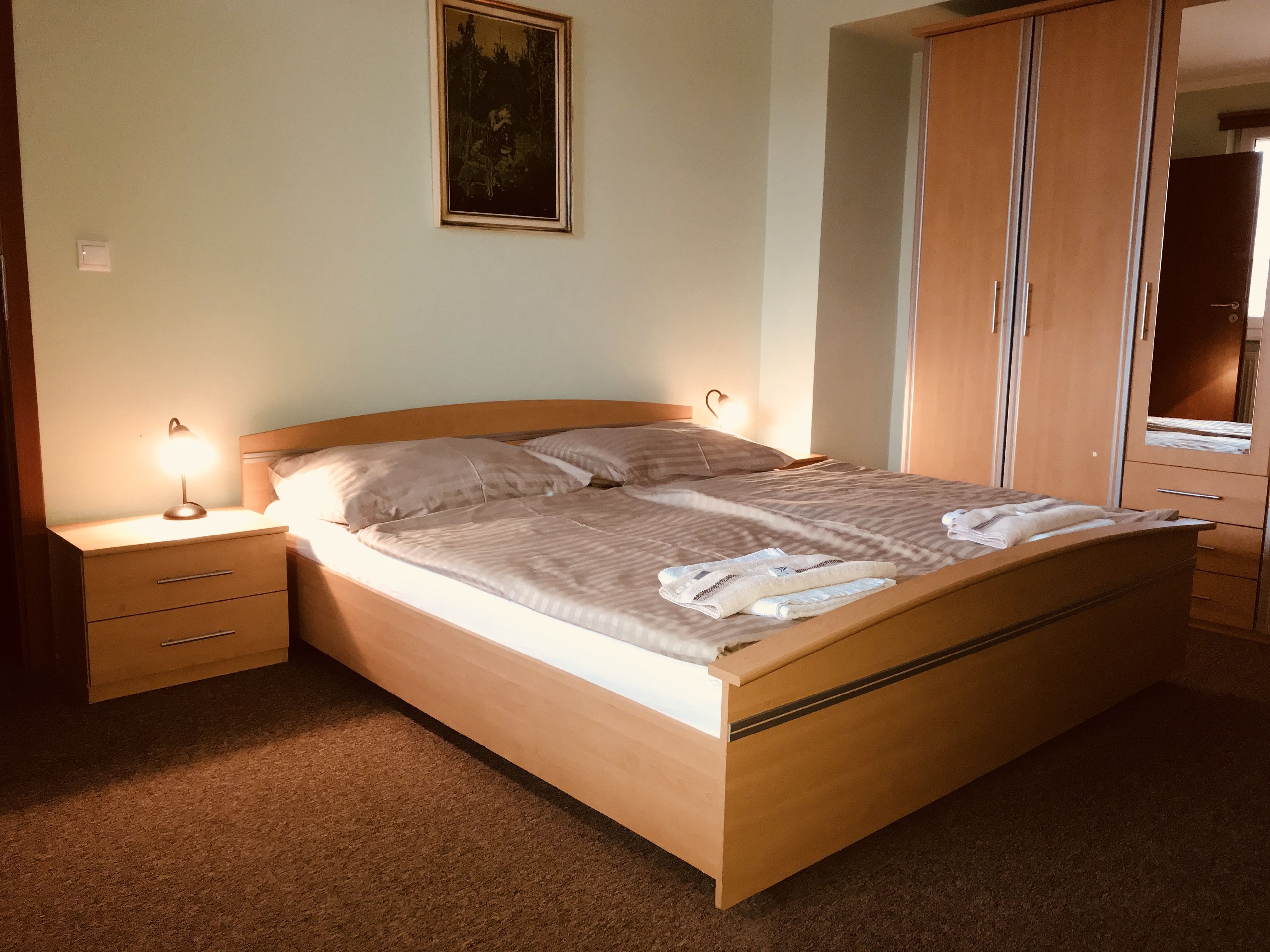Un lit bien fait, avec une tête de lit en bois, une lampe de chevet et une table de chevet.
