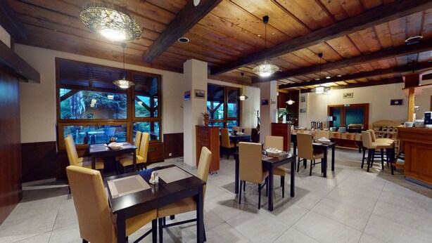 Un restaurante con techos de madera y ventanas amplias que dan a un área boscosa. Mesas y sillas dispuestas para comer.