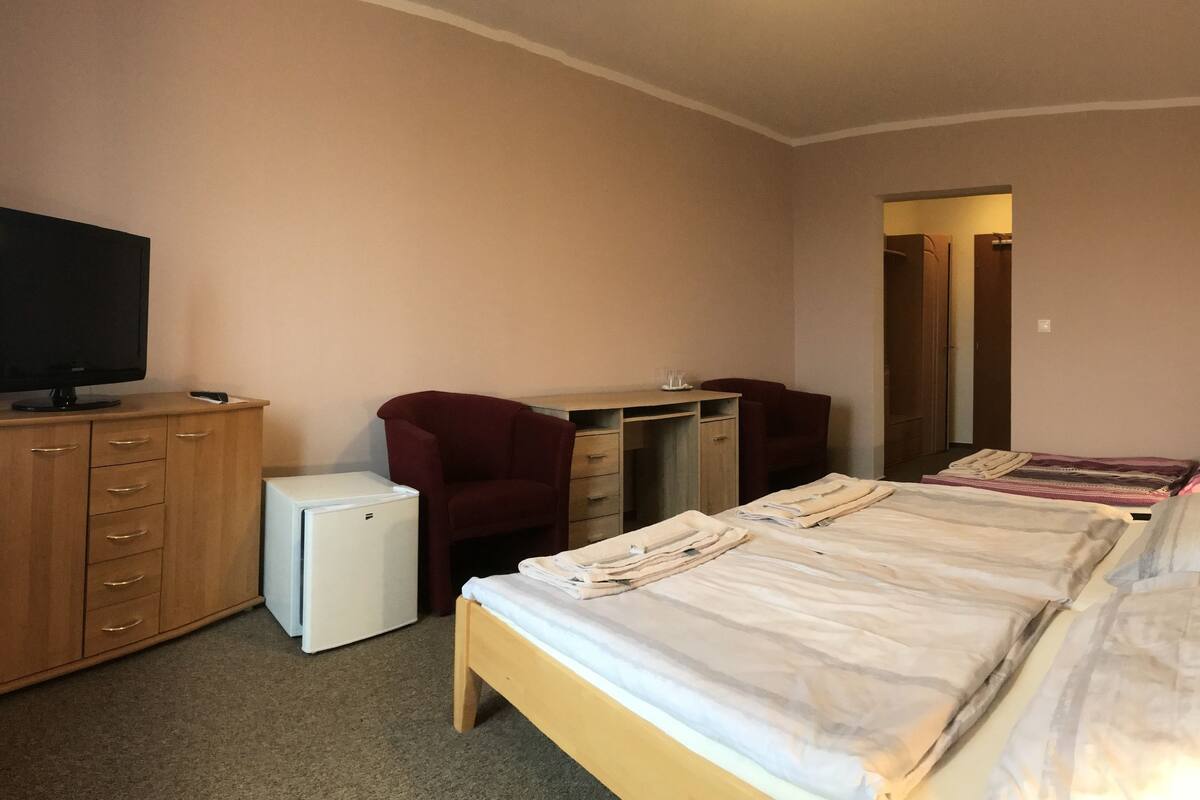 A bedroom with a bed, a desk, a chair, a TV, and a small fridge.