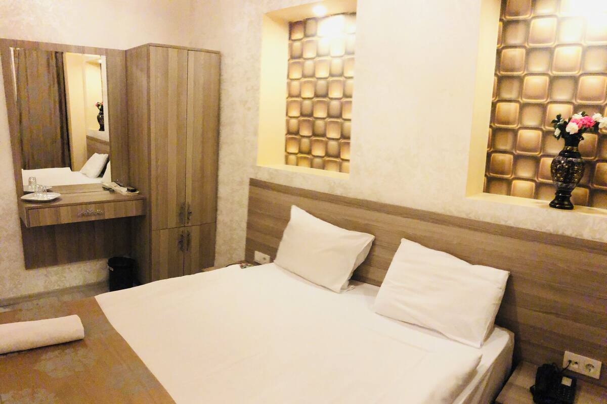 A hotel room with a bed, a bedside table with a phone, a mirror, and a wall with a textured pattern.