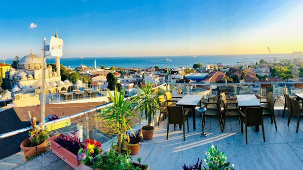 Terraza en la azotea con mesas y sillas, plantas en macetas y vistas a la ciudad y al mar.