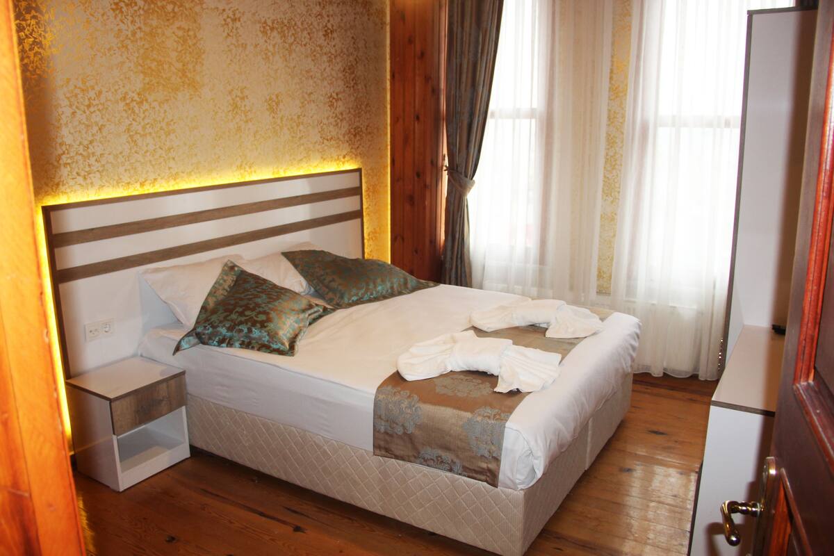 A neatly made bed with pillows and a blanket, a bedside table, and a wooden headboard.
