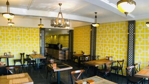 Interior de restaurante con paredes de color amarillo estampado, mesas y sillas de madera, y lámparas colgantes.