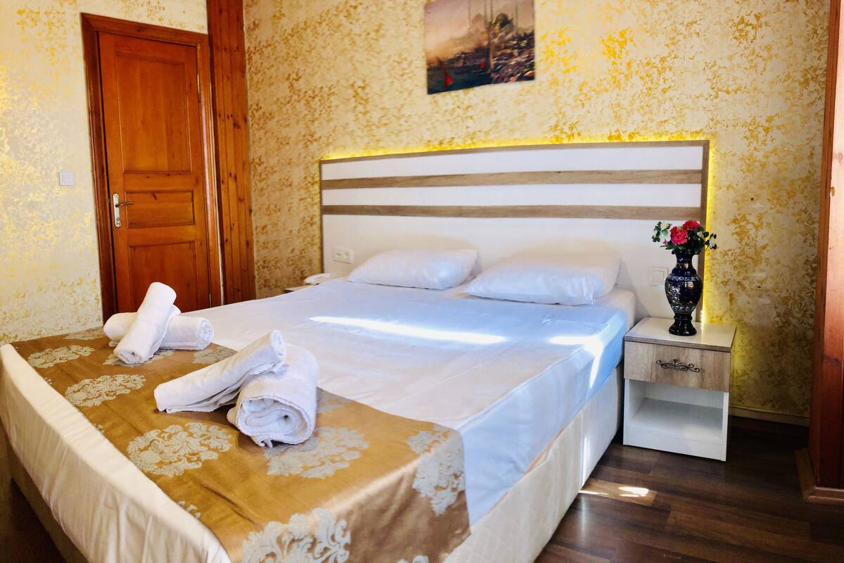 A neatly made bed with white linens, a wooden headboard, and a nightstand with a vase of flowers.