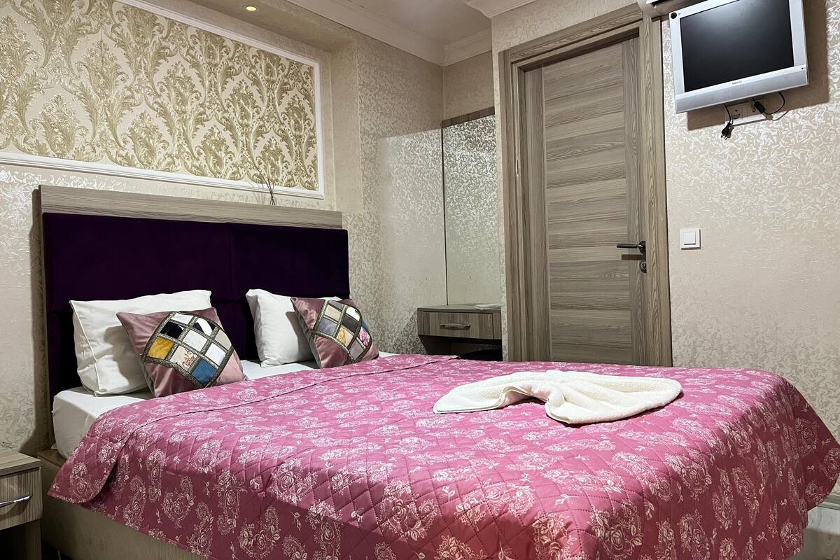 A bedroom with a bed, a TV mounted on the wall, and a wooden wardrobe.