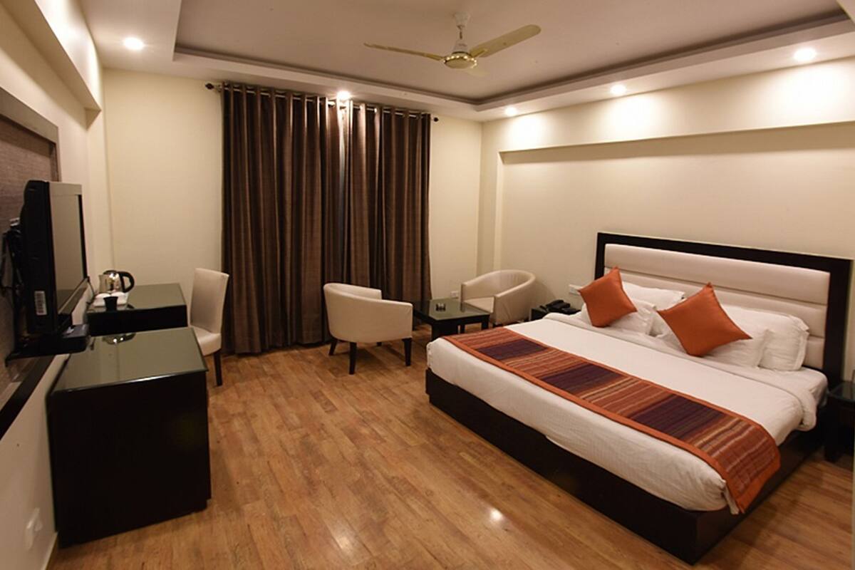 A hotel room with a bed, a desk, two chairs, a television, and a ceiling fan.