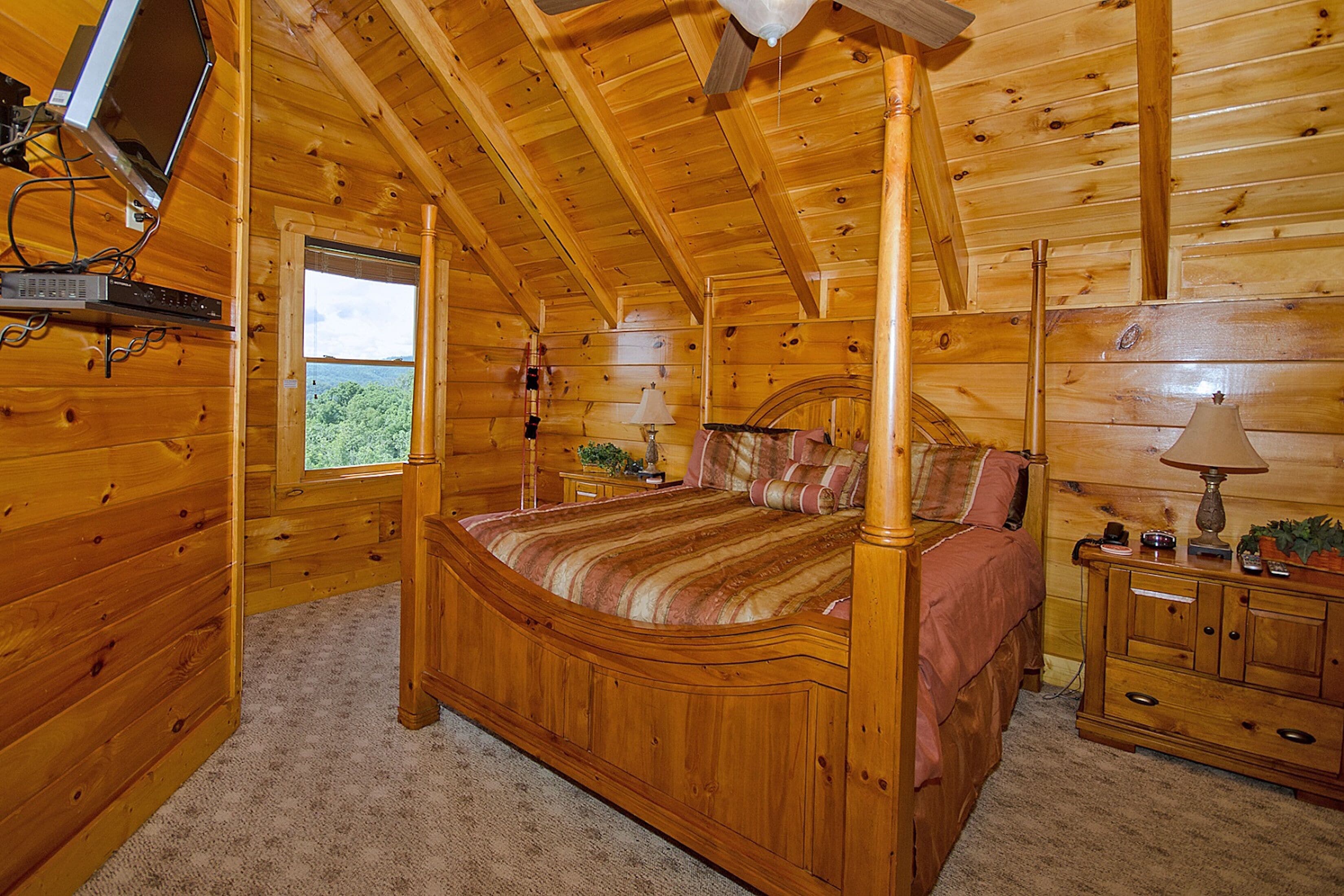 Une chambre à coucher dans un chalet en bois, avec un lit à baldaquin, un téléviseur fixé au mur et une fenêtre donnant sur l’extérieur.