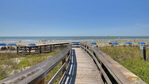 A wooden boardwalk leading to a beach with blue umbrellas. - Coastal Calm- Luxury in the Lowcountry (Kiawah Island)