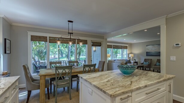 A spacious kitchen with a marble countertop, a large island, and a dining area with a view of the outdoors. - Coastal Calm- Luxury in the Lowcountry (Kiawah Island)