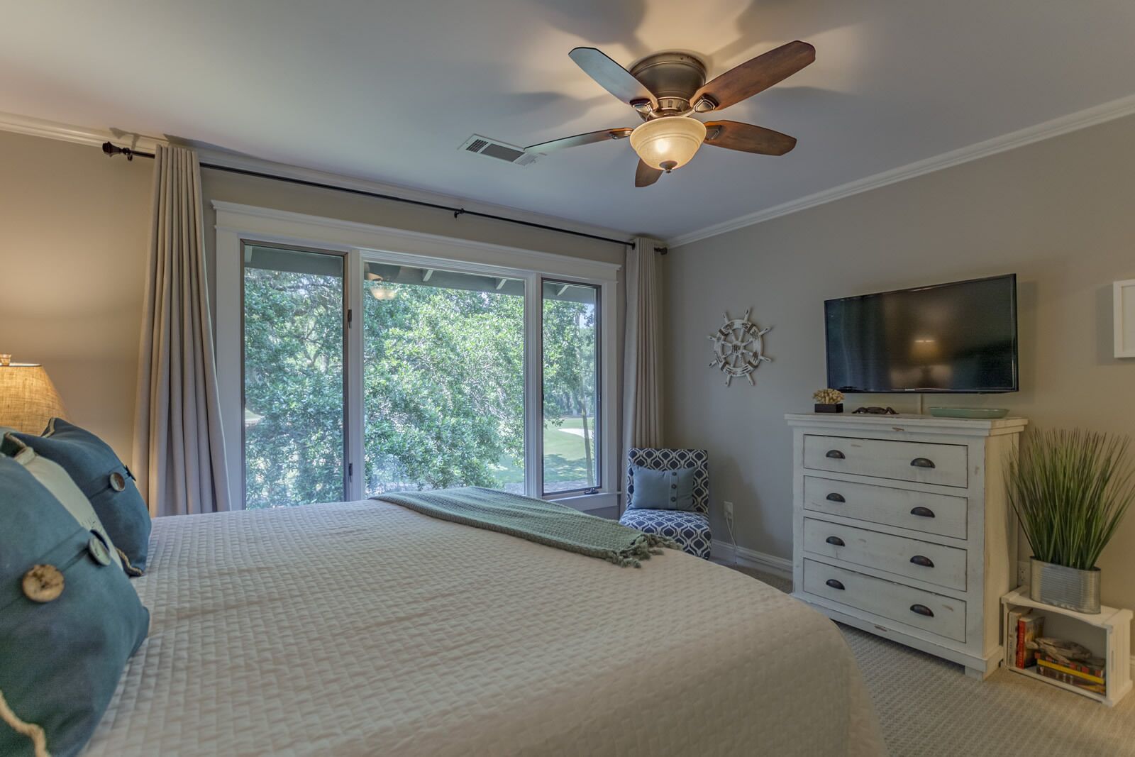 Una camera da letto con un letto, una ventola a soffitto, una TV, una cassettiera e una finestra vista alberi.