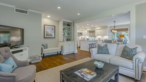 A spacious living room with a television, two sofas, a coffee table, and a kitchen in the background. - Coastal Calm- Luxury in the Lowcountry (Kiawah Island)