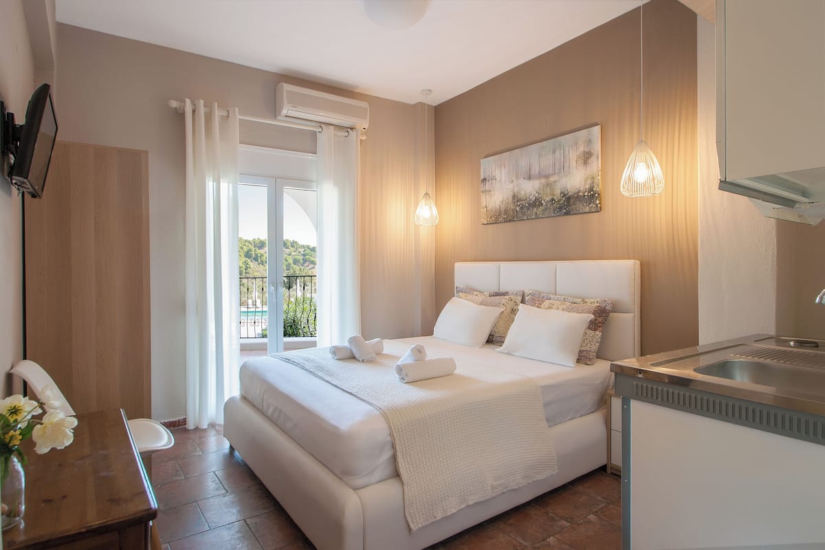 A modern bedroom with a large bed, a desk, and a view of greenery outside.