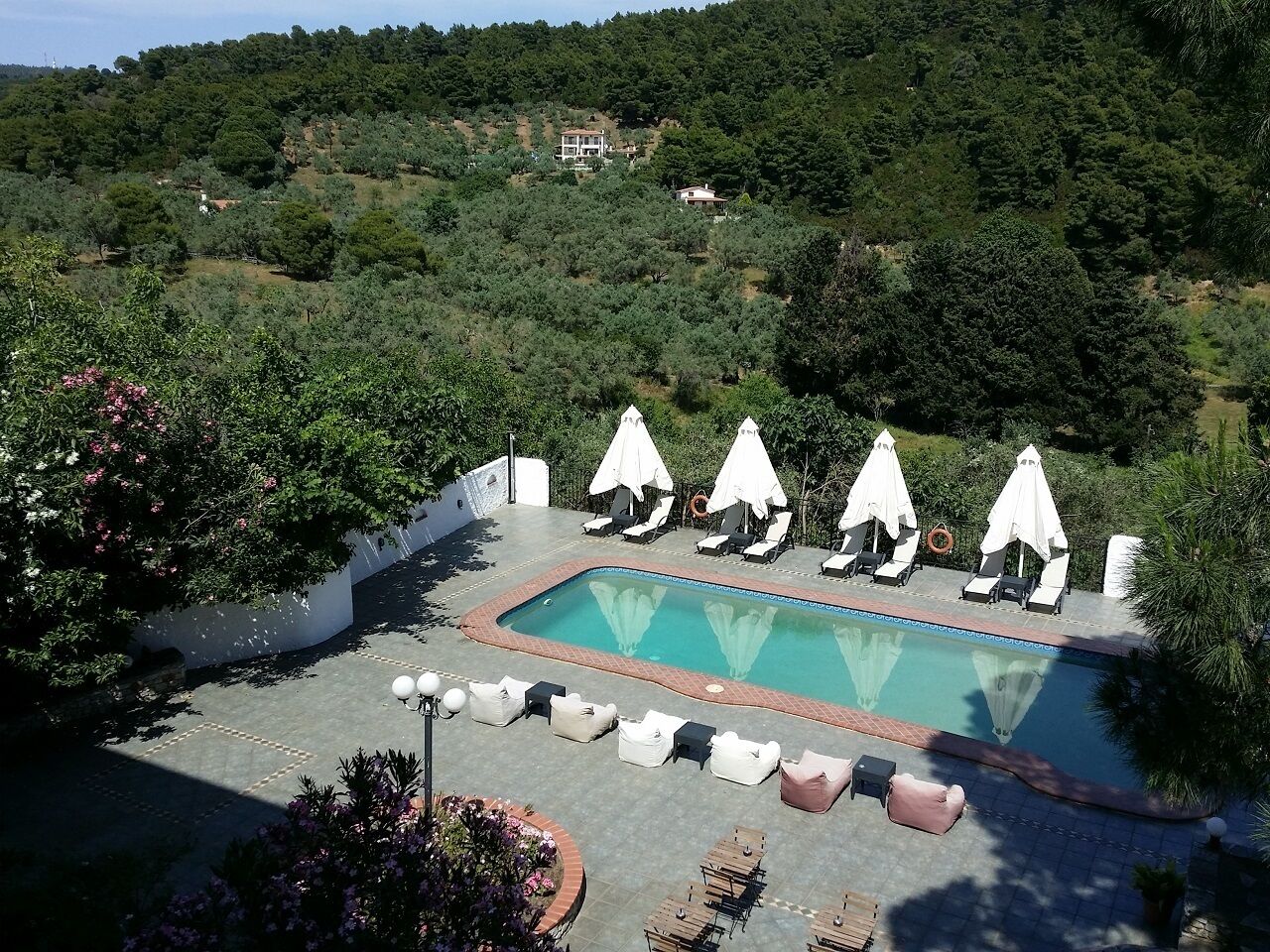 Piscina com espreguiçadeiras e guarda-sóis, rodeada por vegetação e uma encosta.