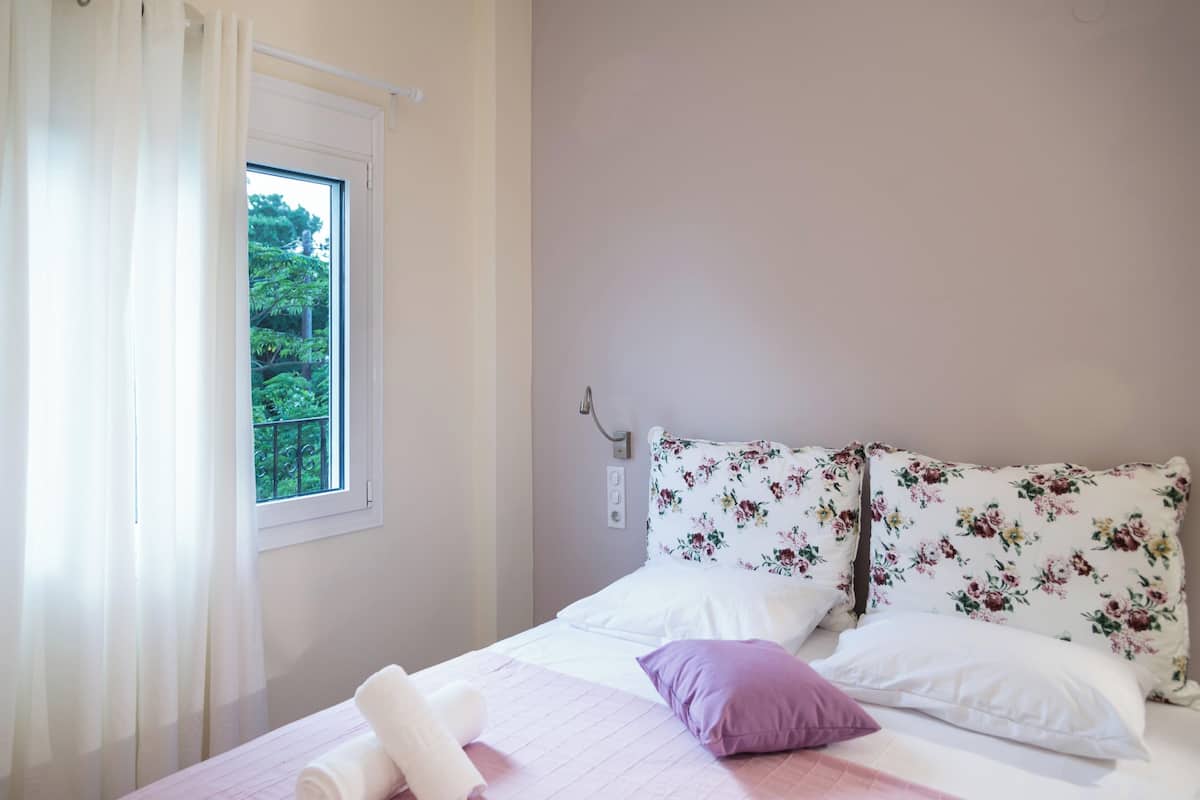 A bedroom with a bed, a window with curtains, and a view of greenery outside.