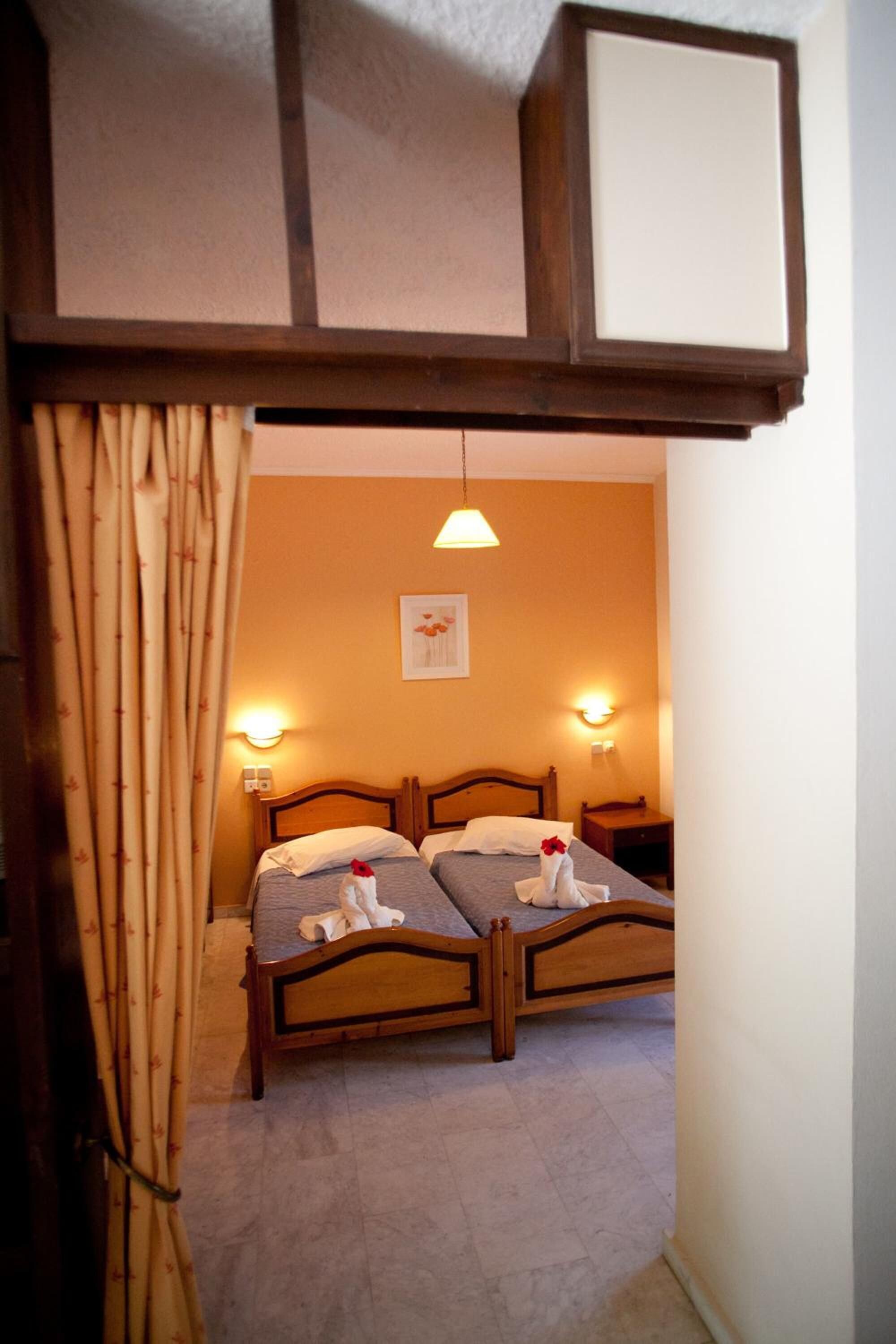A room with two wooden beds, a wall-mounted light fixture, and a framed picture on the wall.