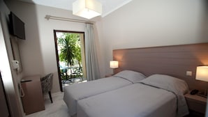 A hotel room with two beds, a TV mounted on the wall, a desk with a telephone, and a view of the outdoors through a glass door. - Kalydna Island Hotel (Kalymnos)