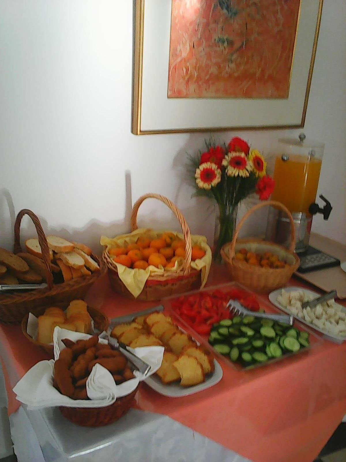Una mesa de buffet con diferentes alimentos, como pan, frutas, verduras y un dispensador de zumo.