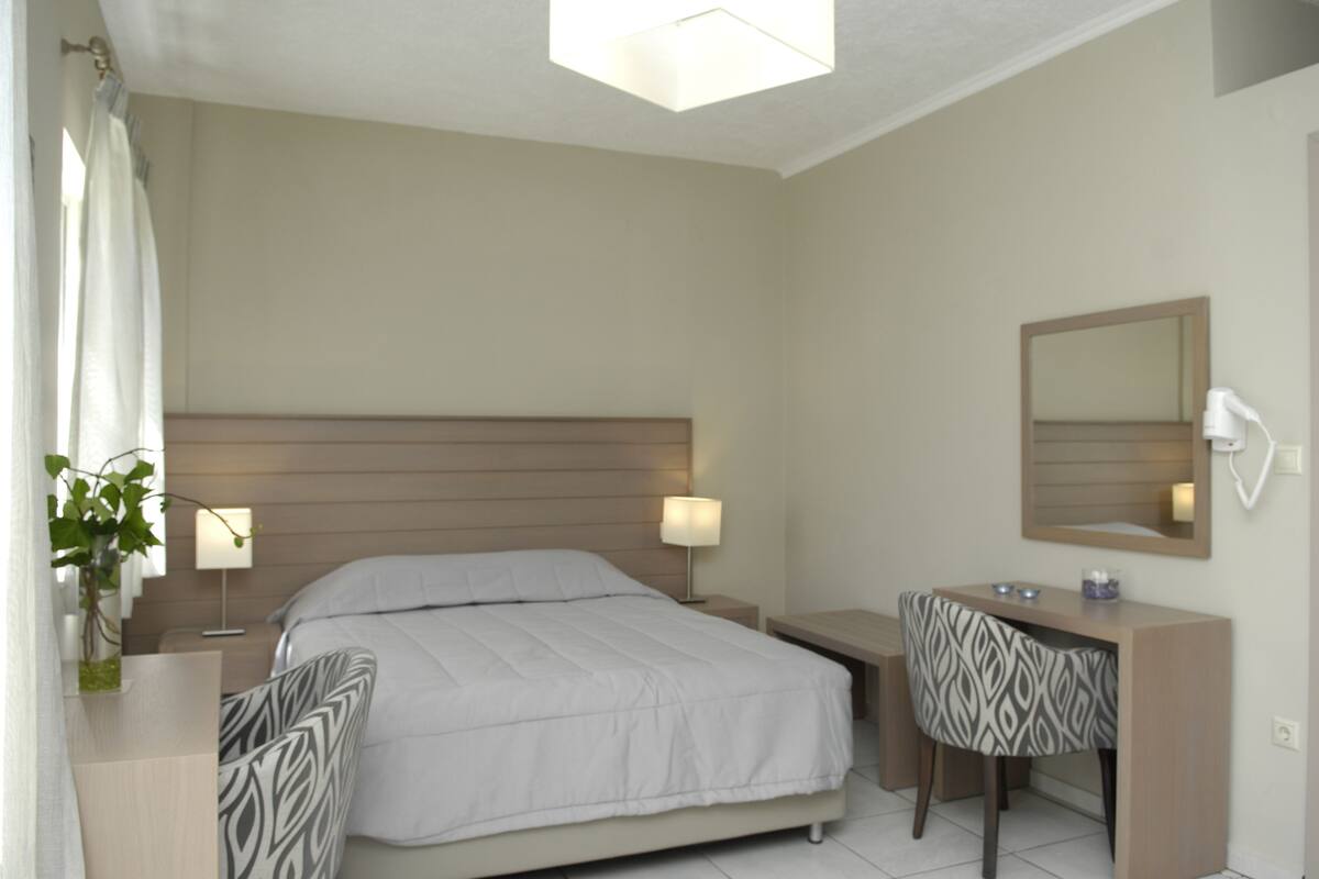 A bedroom with a bed, bedside tables, a desk with a chair, a mirror, and a potted plant.