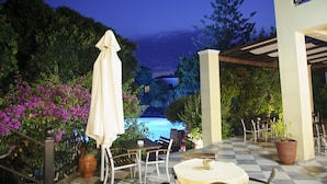 An outdoor patio area with tables and chairs, a covered seating area, and a view of a swimming pool. - Kalydna Island Hotel (Kalymnos)