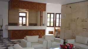 A spacious living area with a high ceiling, a kitchen with wooden cabinets, and a checkered floor. - Kalydna Island Hotel (Kalymnos)
