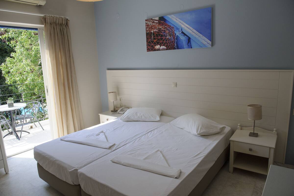 A double bed with white linens, a bedside table with a lamp, and a painting on the wall.