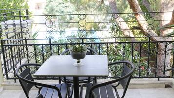 A balcony with a table and chairs, a potted plant, and a view of trees and a building.