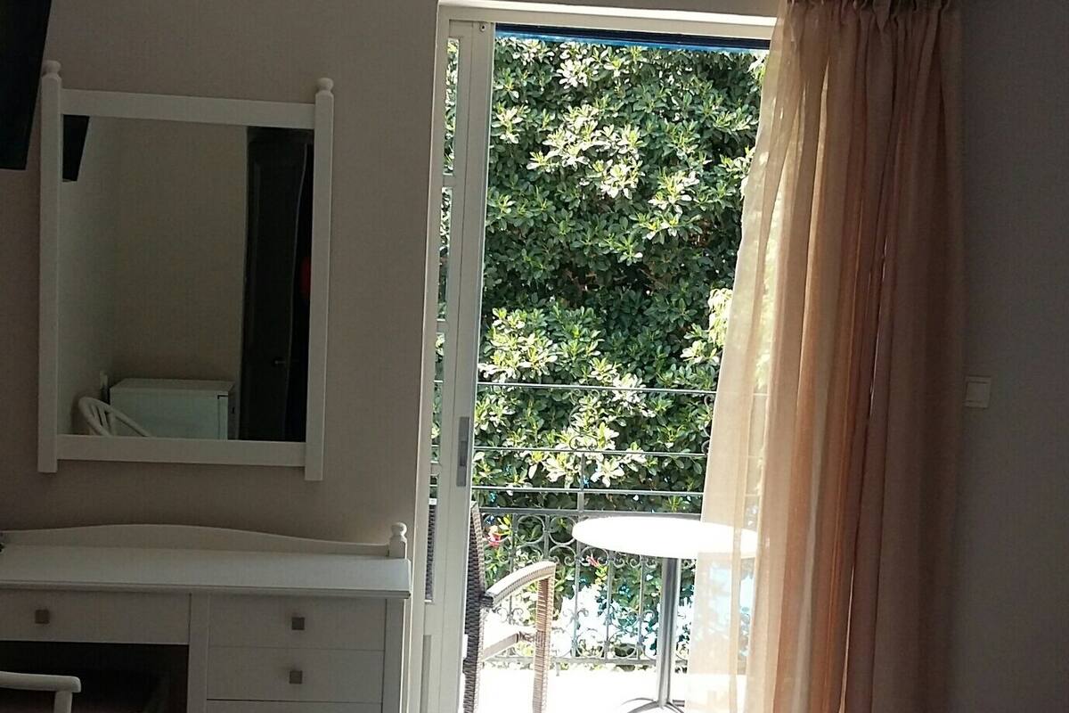 A bedroom with a bed, a desk, a chair, a mirror, and a window with curtains.