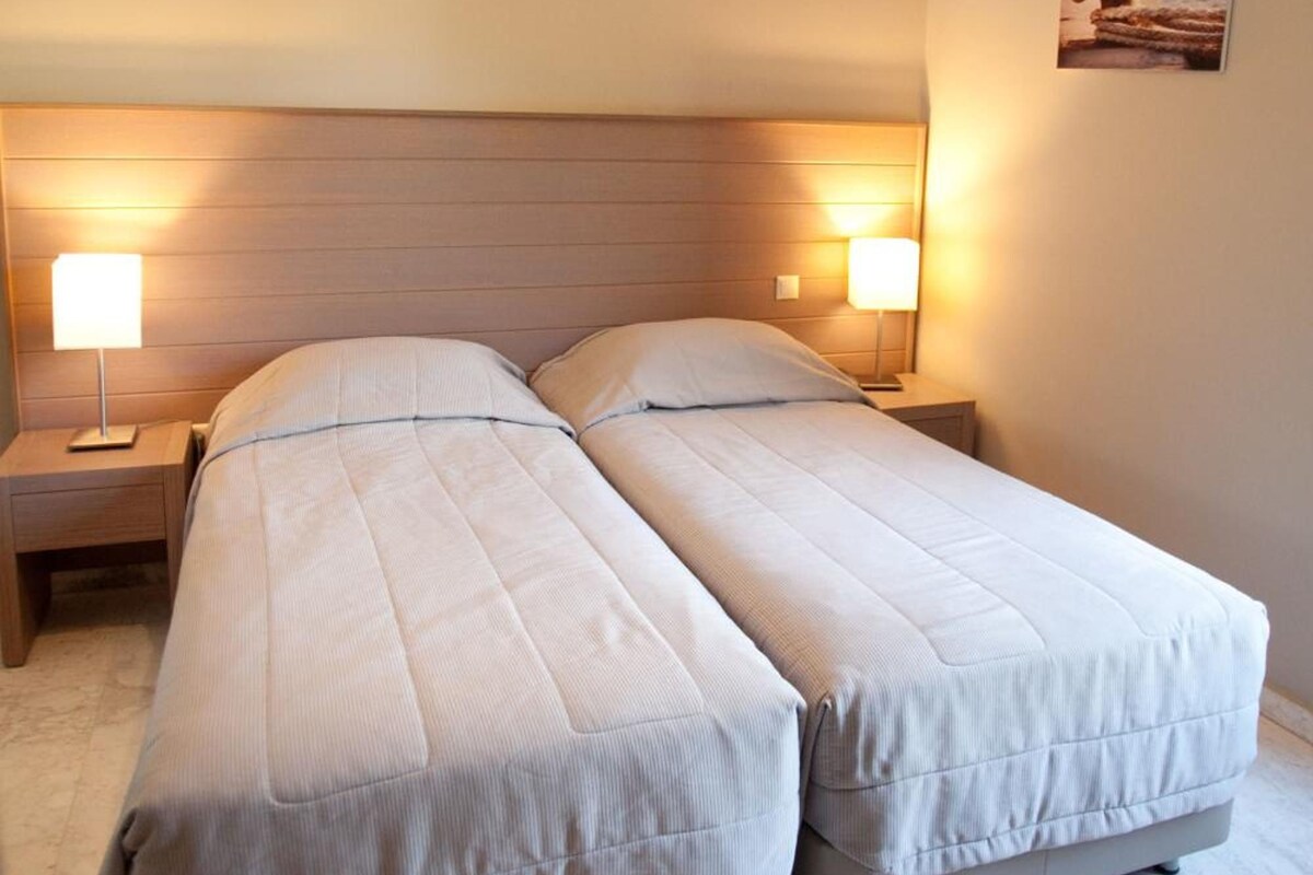 A double bed with two bedside tables, each with a lamp, in a room with a wooden headboard and a single hanging light fixture.