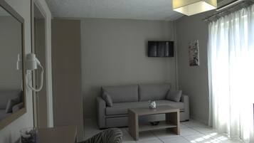 Ein modernes Wohnzimmer mit grauem Sofa, einem Couchtisch, einem an der Wand befestigten Fernseher und einem Fenster mit Vorhängen.