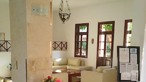 A lobby with a checkered floor, a sofa, a table with a vase of flowers, and a bulletin board. - Kalydna Island Hotel (Kalymnos)
