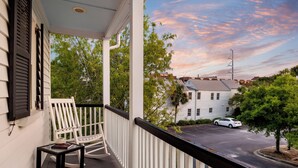 A porch with a rocking chair and a table, overlooking a street with houses and a car. - Cozy Charleston Cottage | Brandy Crusta (Charleston)
