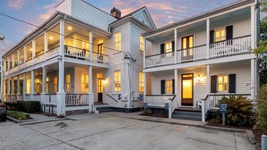 A two-story white building with balconies and a covered front porch. - Cozy Charleston Cottage | Brandy Crusta (Charleston)