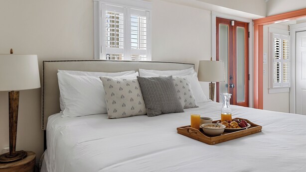 A neatly made bed with a tray of breakfast including cereal, fruit, and juice, and two bedside lamps. - Cozy Charleston Cottage | Brandy Crusta (Charleston)