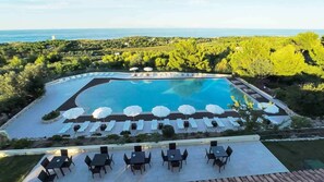Un resort con una amplia piscina rodeada de tumbonas y sombrillas, con vistas a la costa.