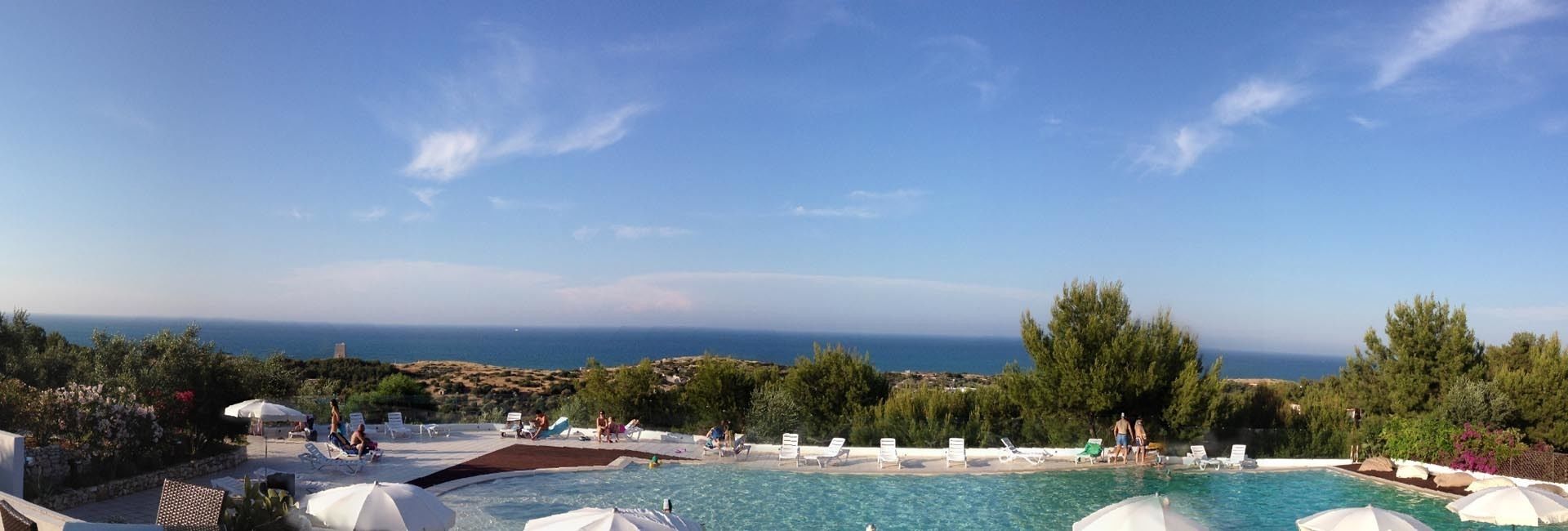 A pool area with lounge chairs and umbrellas, overlooking a scenic view of the sea and hills.