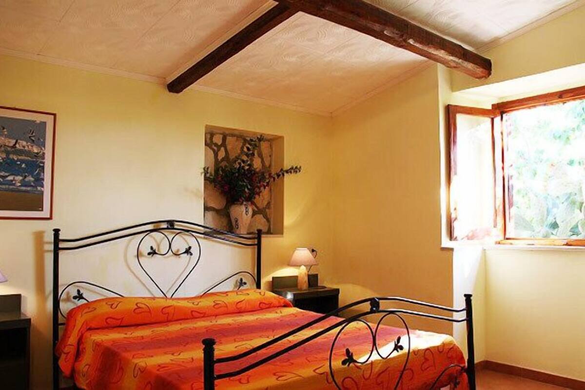 A bedroom with a bed, a nightstand, a lamp, a painting, and a window with a view.