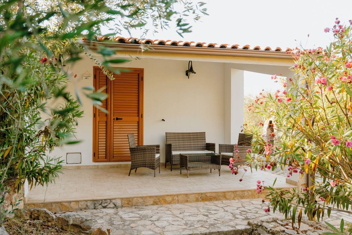 A covered outdoor seating area with wicker furniture, a stone pathway, and a building entrance with a wooden door.
