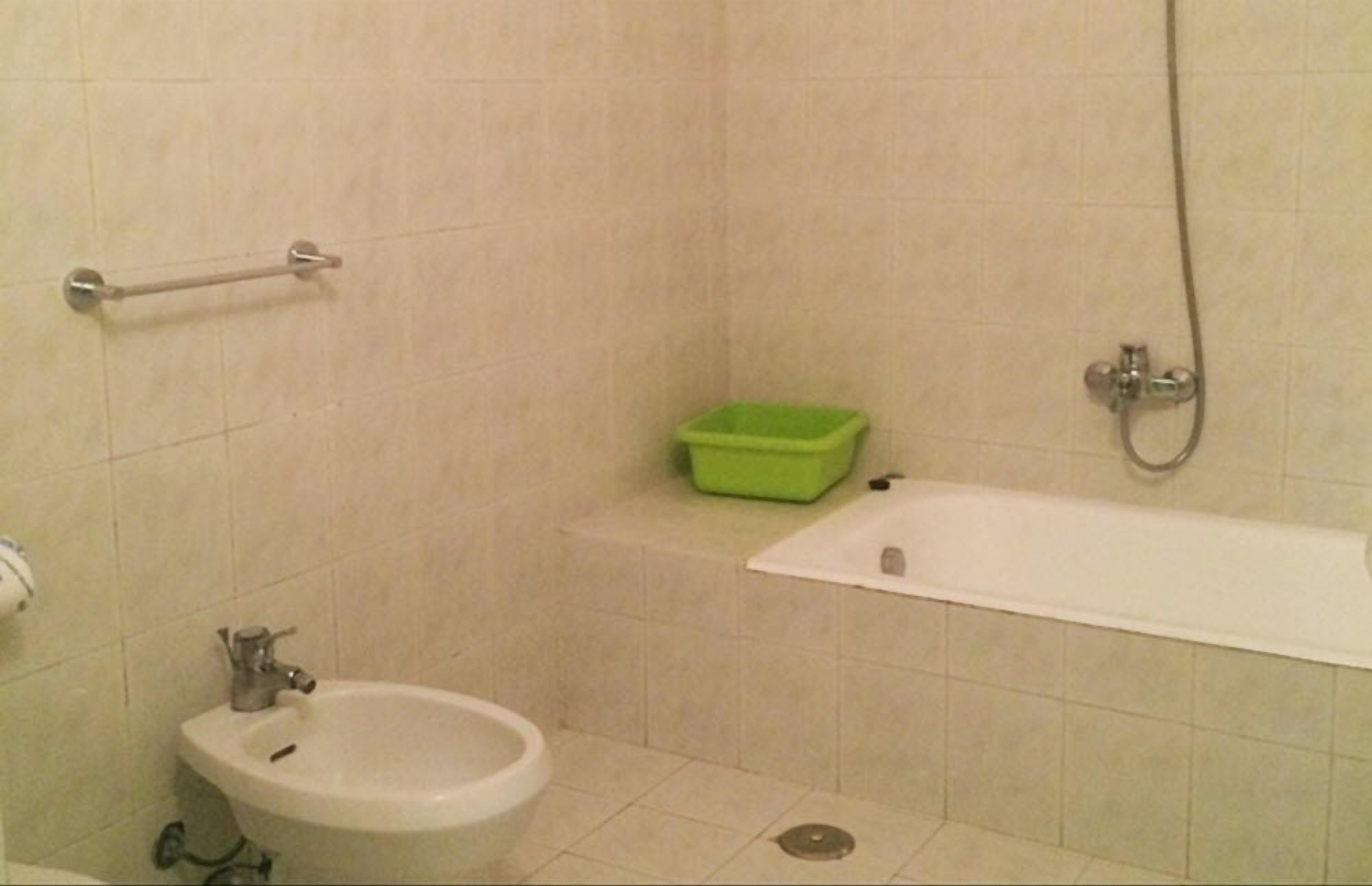 Een badkamer met een hygiëneschuimer, toilet, groene prullenbak en bad.