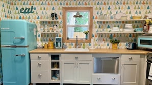 A kitchen with a vintage blue refrigerator, a window above the sink, and a wall with a pear pattern. - Retro, Cozy Cottage - Peninsula St. Park, Family/Pet Friendly - OPEN year around (Fish Creek)