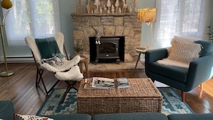 A cozy living room with a stone fireplace, a blue armchair, a fluffy chair, and a coffee table with magazines. - Retro, Cozy Cottage - Peninsula St. Park, Family/Pet Friendly - OPEN year around (Fish Creek)