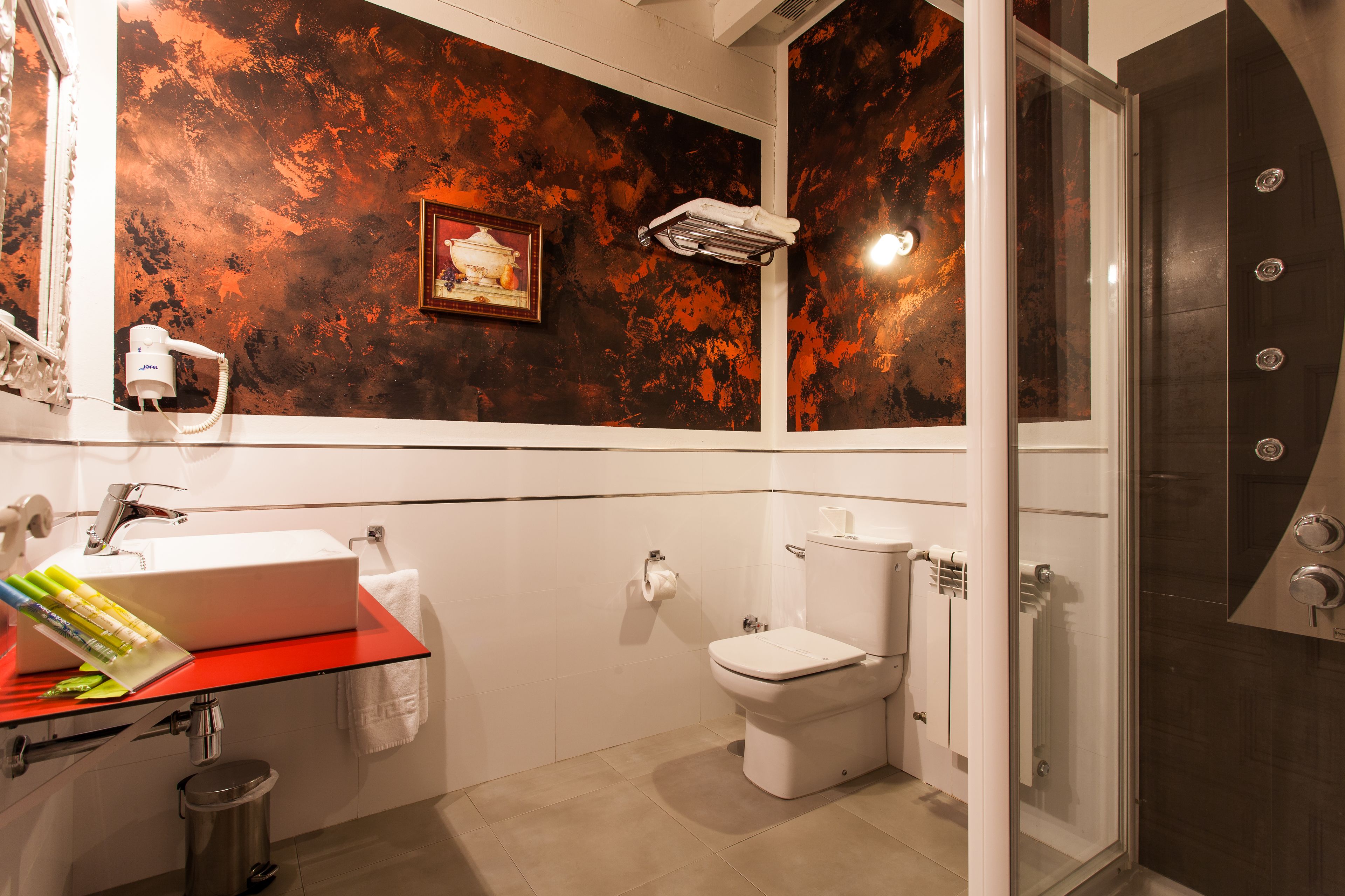 A bathroom with a red countertop sink, a white toilet, and a shower area.