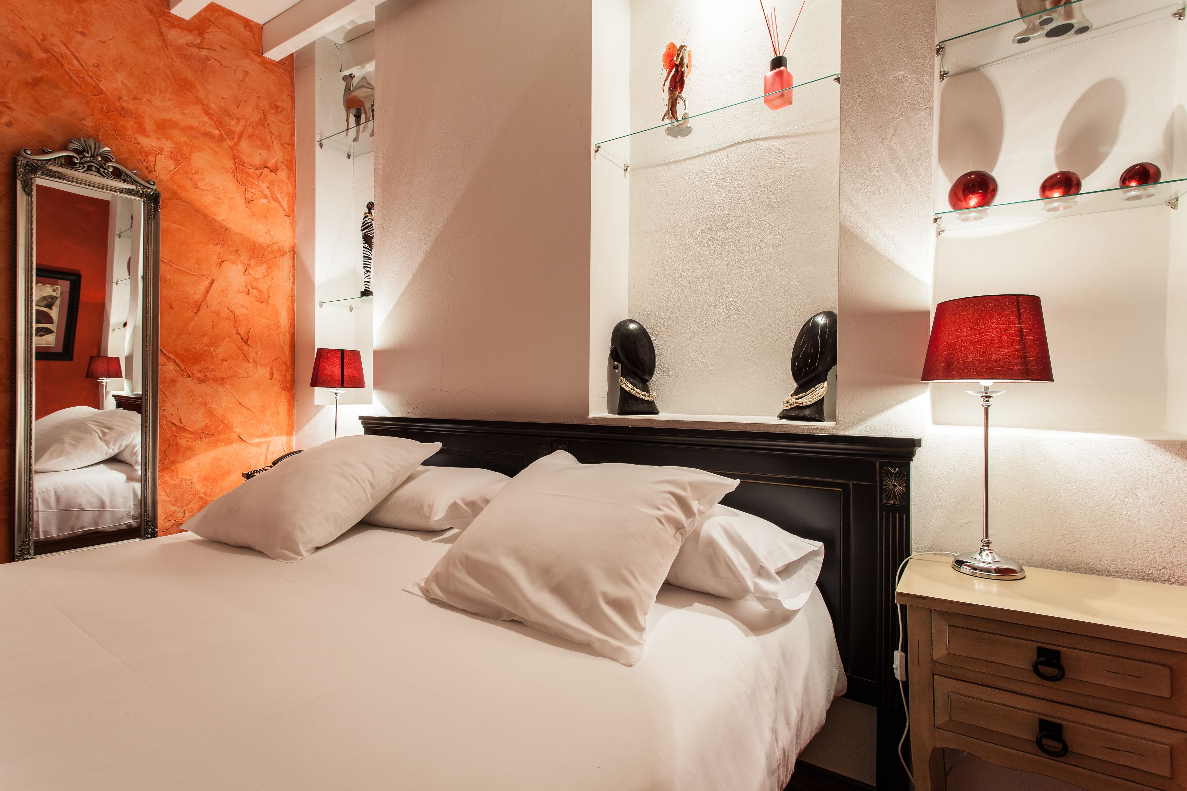 A hotel room with a bed, a nightstand, a mirror, and a wall with decorative items.
