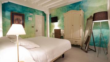 A bedroom with a bed, a bedside lamp, a wardrobe, a television, and a mirror on a stand.