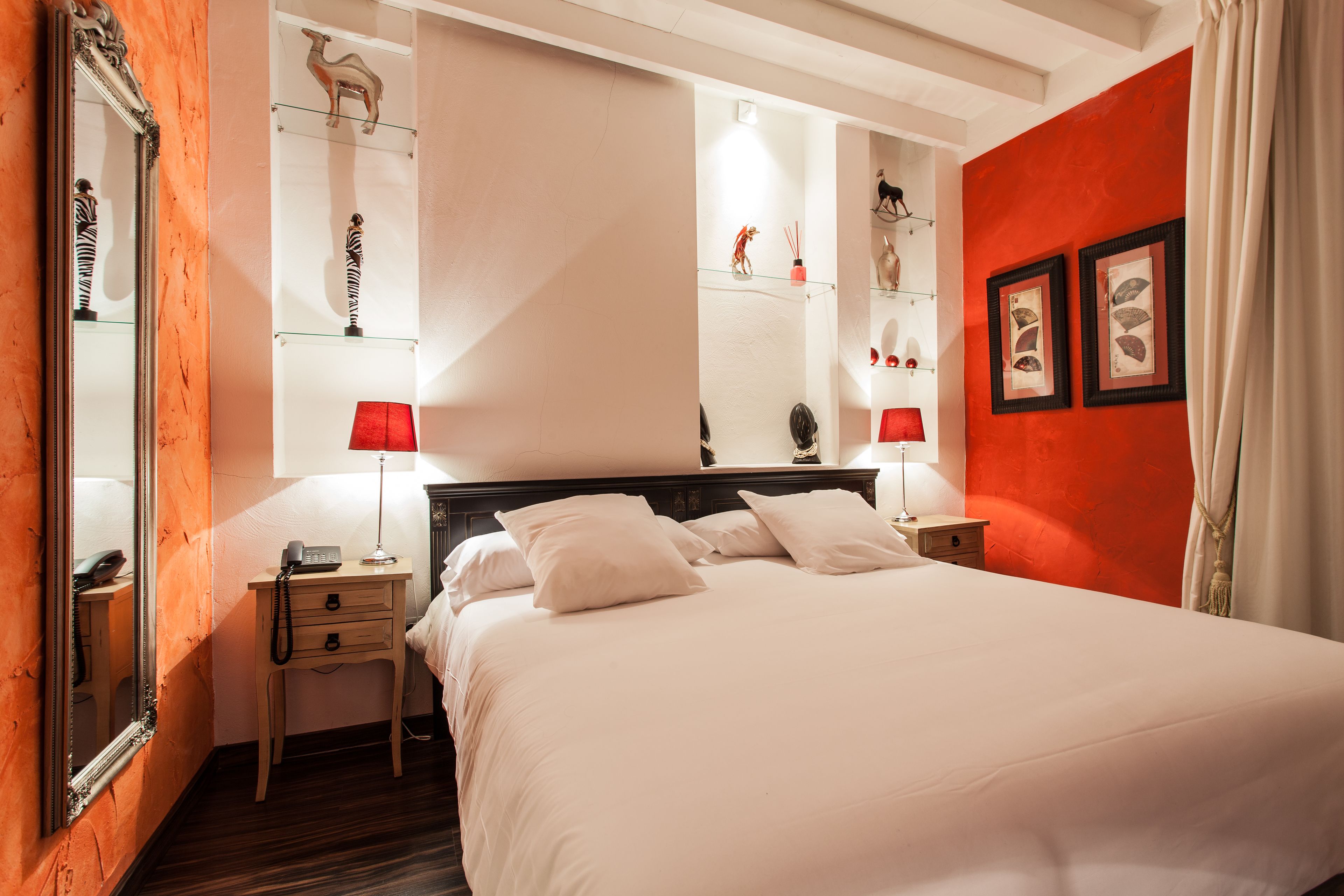 A hotel room with a large bed, two bedside tables, a mirror, and a red accent wall.