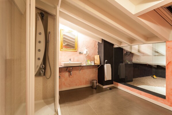 Un baño moderno con cabina de ducha de vidrio, un lavabo con espejo encima y una bañera negra visible a través de una mampara de cristal.