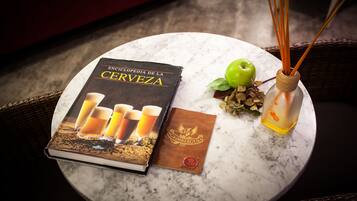 A book titled 'Encyclopedia de la Cerveza' on a round table, a green apple, and a reed diffuser with orange peels.