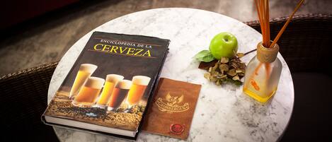 A book titled 'Encyclopedia de la Cerveza' on a round table, a green apple, and a reed diffuser with orange peels.