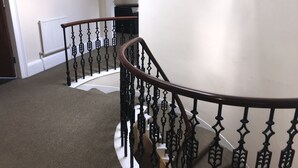 Eine Treppe mit Holzhandlauf und schwarzen Spindeln, mit Teppich belegten Stufen, einer weißen Wand und einem Heizkörper.