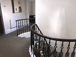 A staircase with a wooden handrail and black balusters, carpeted steps, a white wall, and a radiator.